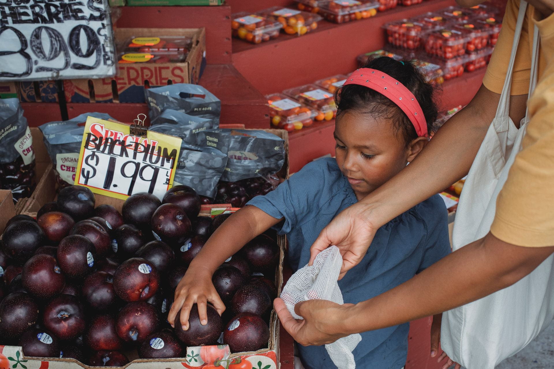 Little girl picks up plums at a local market